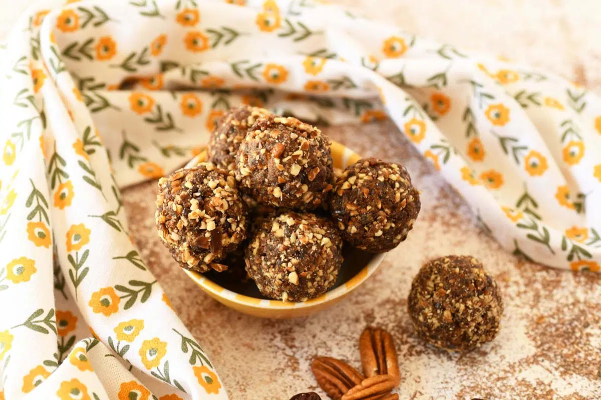 Pecan coated energy balls in a yellow dish with a floral napkin nearby.