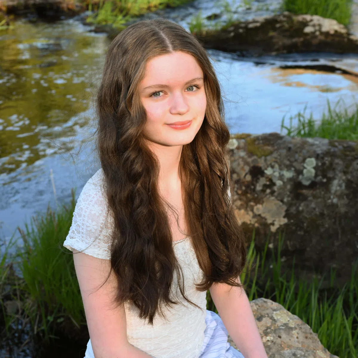 A girl with wavy hair outside near a pond.