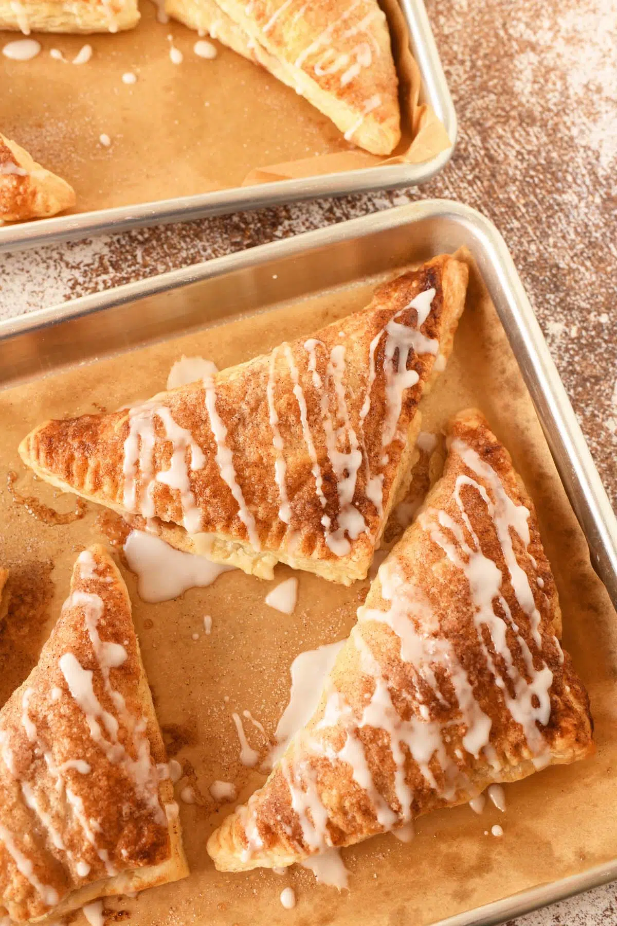 Iced apple turnovers on a parchment-lined baking sheet.