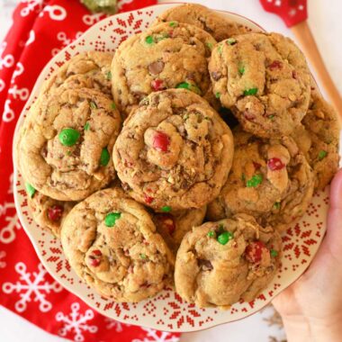 A hand holding a plate of holiday themed red, and green M&M cookies.