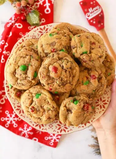 A hand holding a plate of holiday themed red, and green M&M cookies.