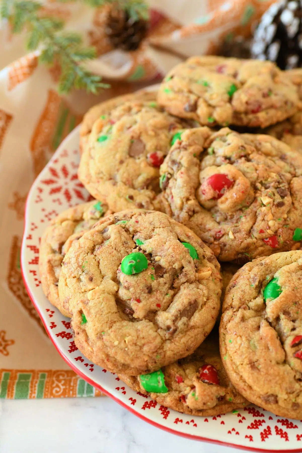 Red, and green M&M Cookies on a holiday patterned red and white plate.