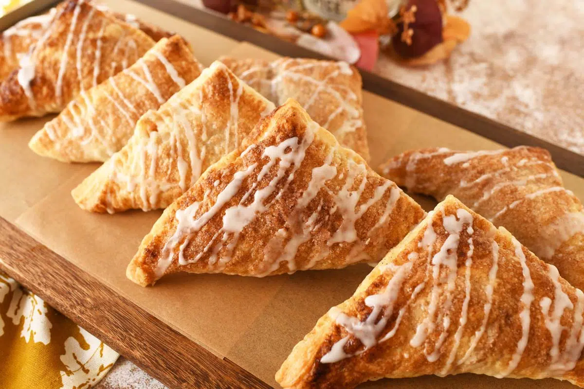 Iced apple turnovers on a wooden parchment-lined serving tray.