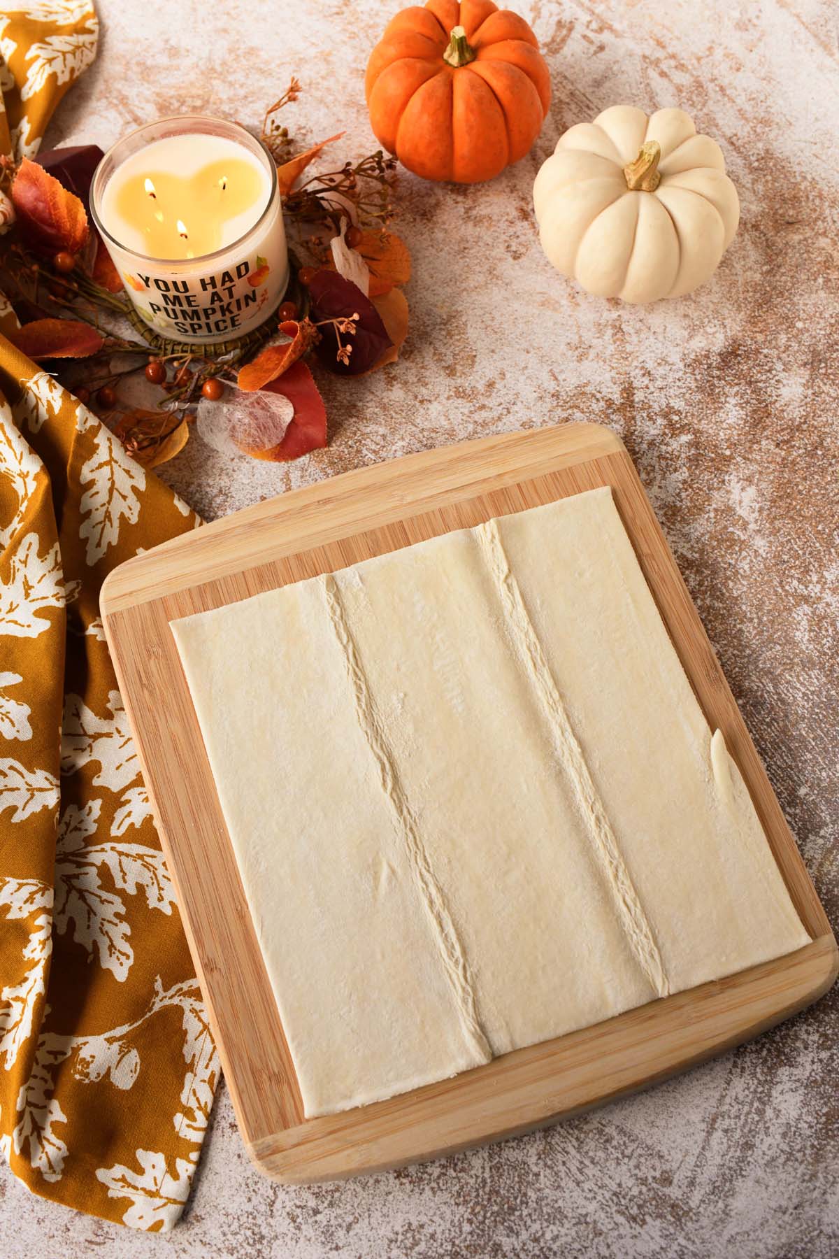 Puff pastry on a wooden cutting board on a fall themed table.