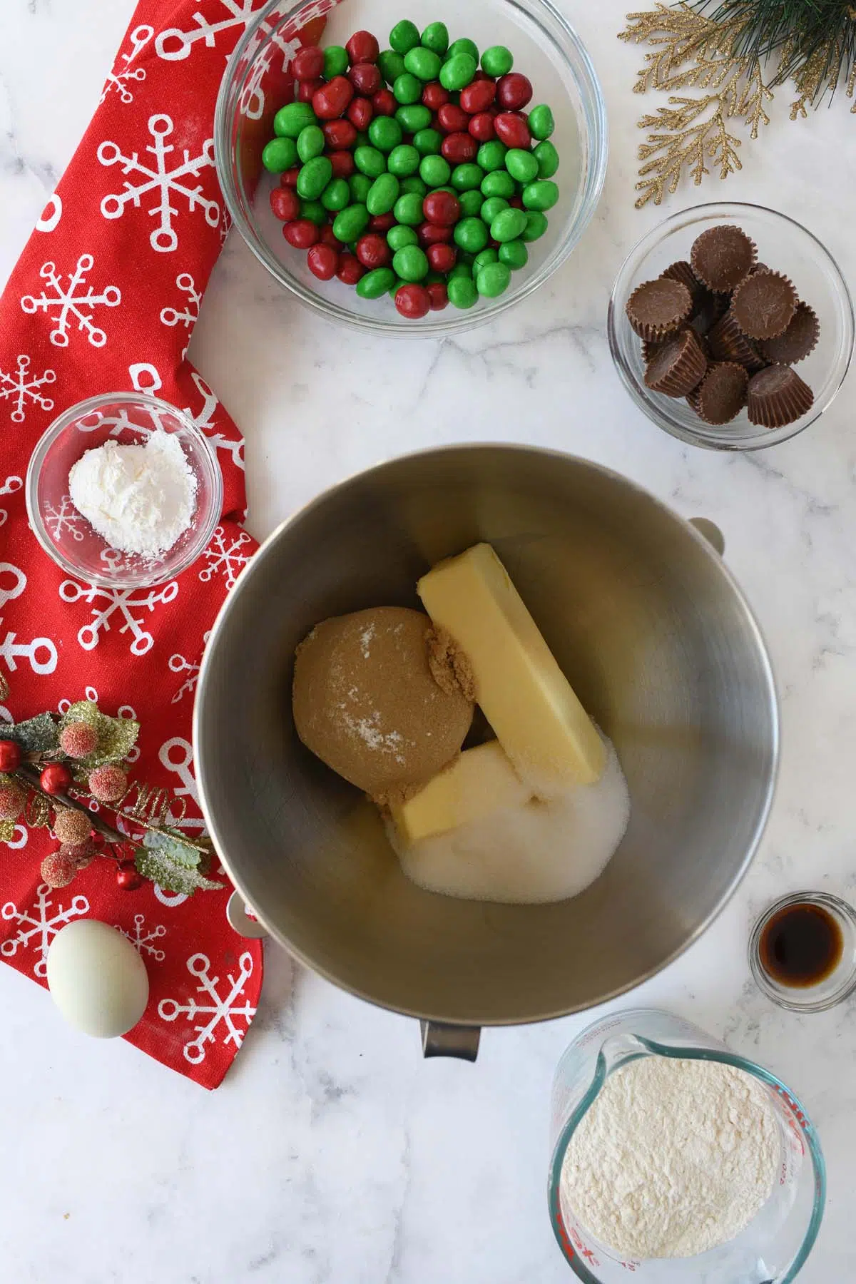 Brown sugar and butter in a stainless steel mixing bowl near a red snowflake napkin and red, and green M&Ms.
