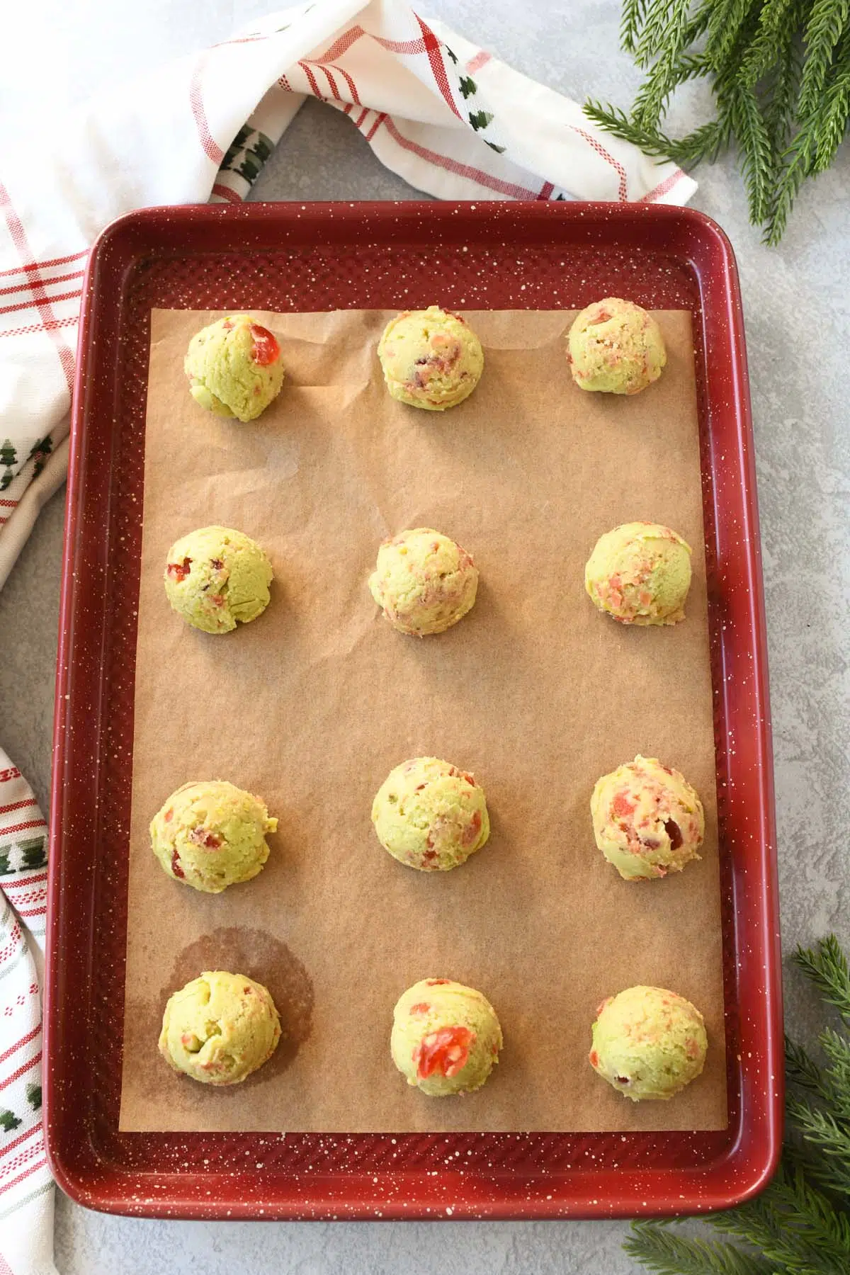 Pistachio cherry cookie balls on a parchment-lined red baking sheet.