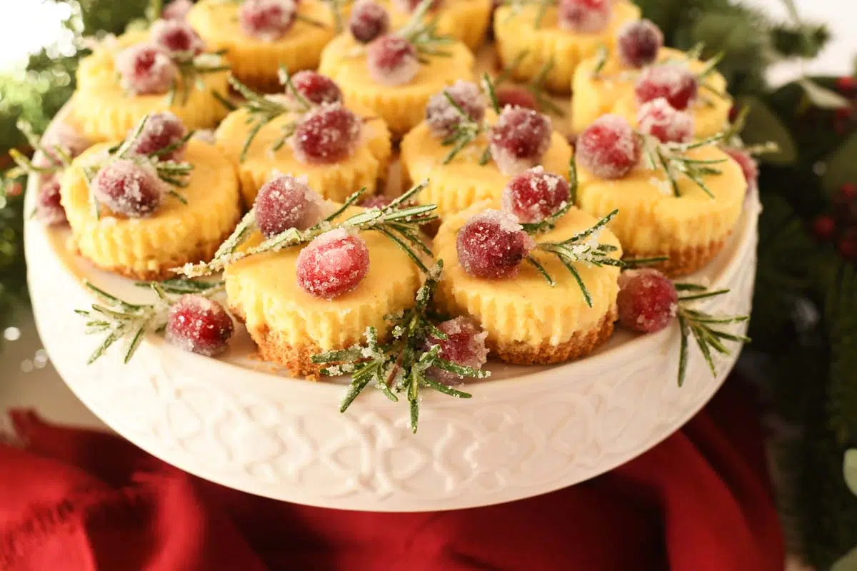 Shot of festive mini cheesecakes on a white platter near a red napkin.