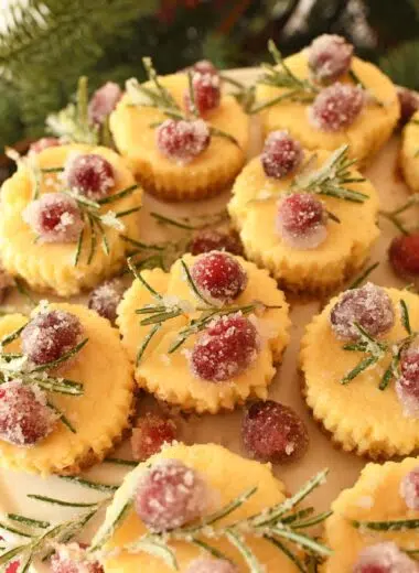 Mini eggnog cheesecakes topped with festive sugared cranberries and rosemary.