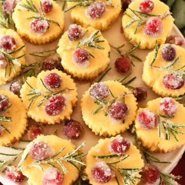 Mini eggnog cheesecakes with sugar rosemary and cranberries on a white platter.
