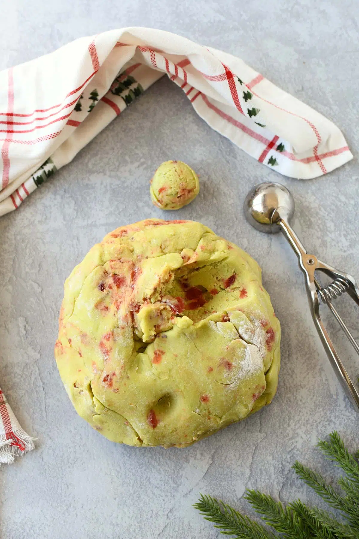Pistachio cherry cookie dough with a cookie scoop and holiday napkin.