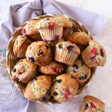 Berry muffins in a basket near a purple napkin.