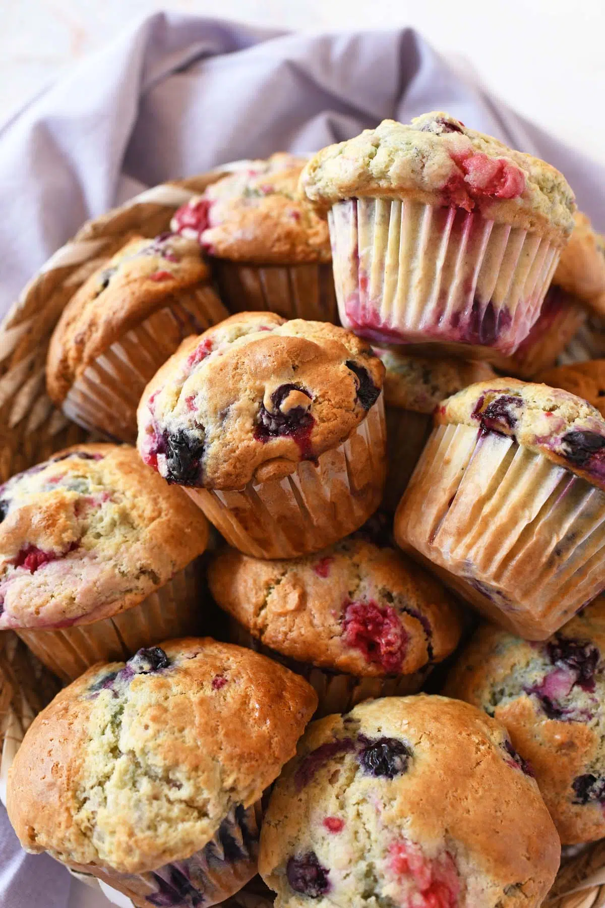 Berry sourdough muffins stacked in a basket near a purple napkin.