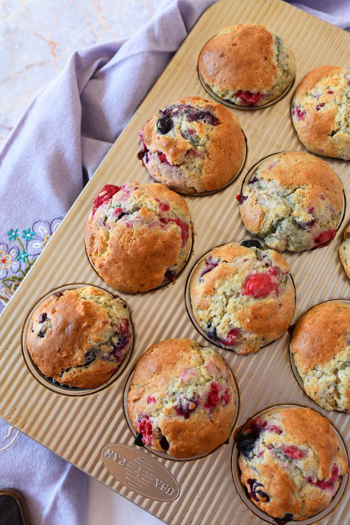 Golden brown berry sourdough muffins with a purple napkin.