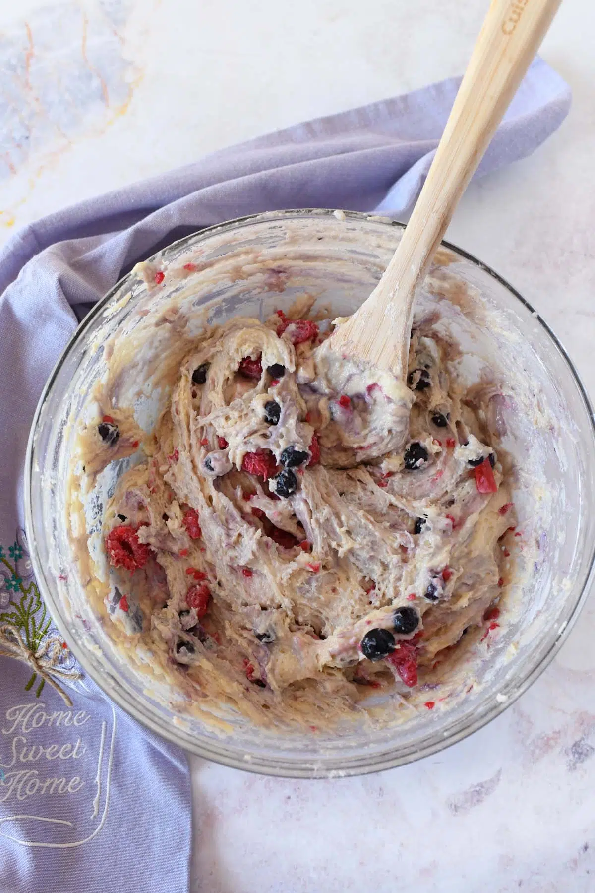 sourdough batter with berries in it with a wooden spoon in a glass dish with a purple napkin.