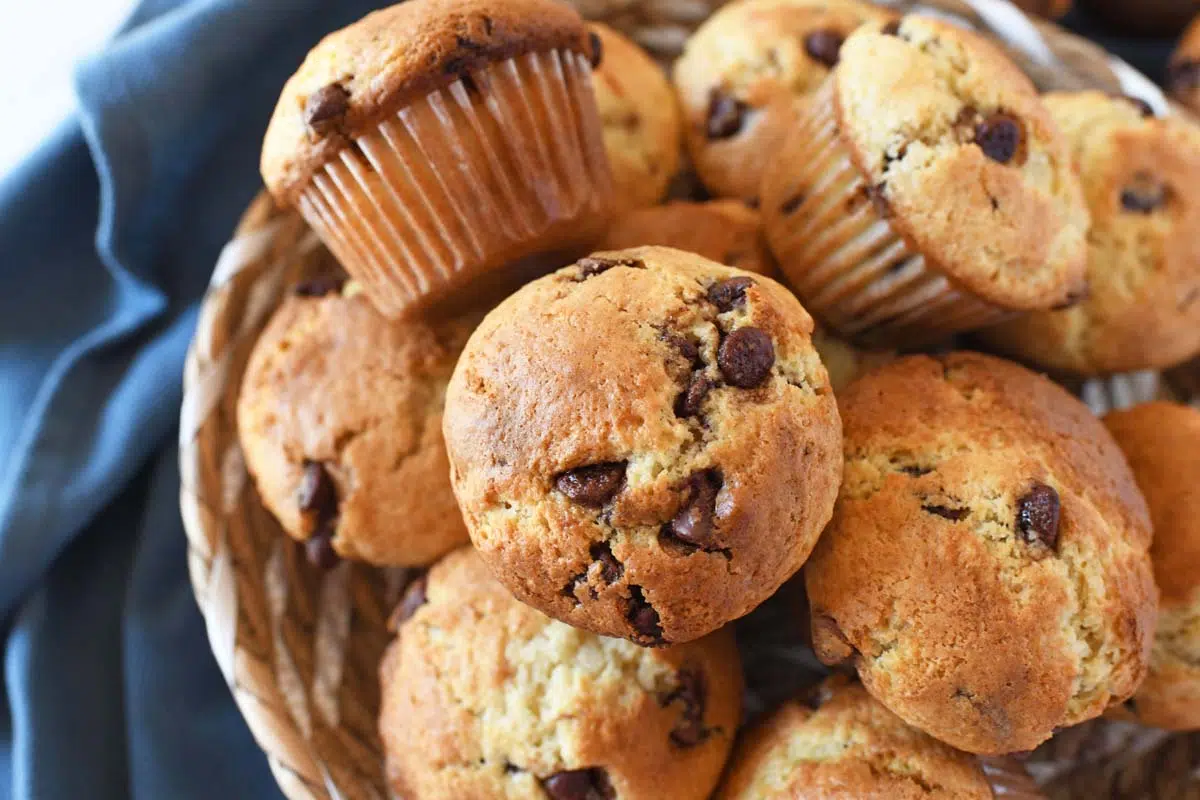 golden brown chocolate chip muffins in a basket near a blue napkin.
