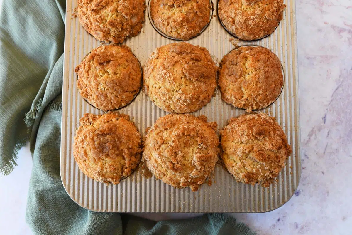 Coffee cake sourdough muffins in a silver muffin tin near a green napkin.
