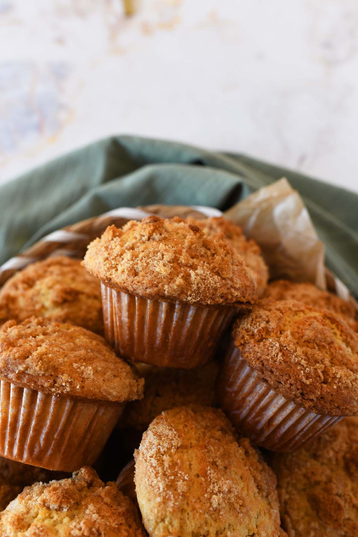 Golden-brown coffee cake muffins in a basket near a green napkin.