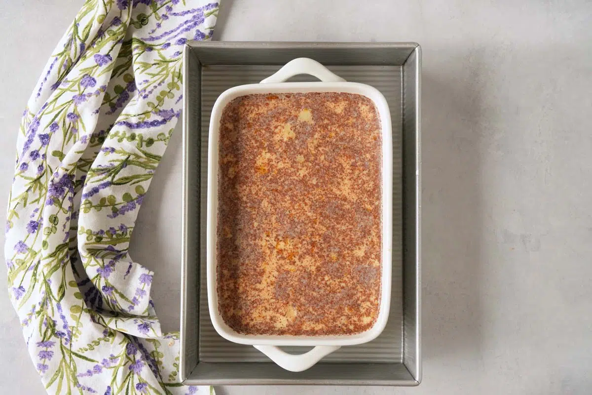 Grape-Nuts pudding batter in a water bath near a purple, floral napkin.