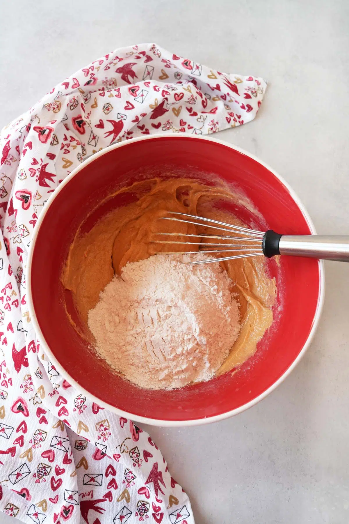 A red bowl of batter with a valentines day napkin nearby.