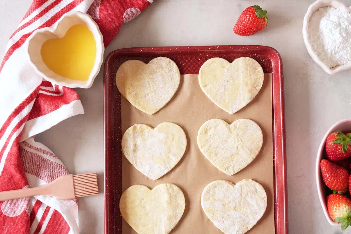 Strawberry Puff Pastry hearts on a red baking sheets near ingredients.