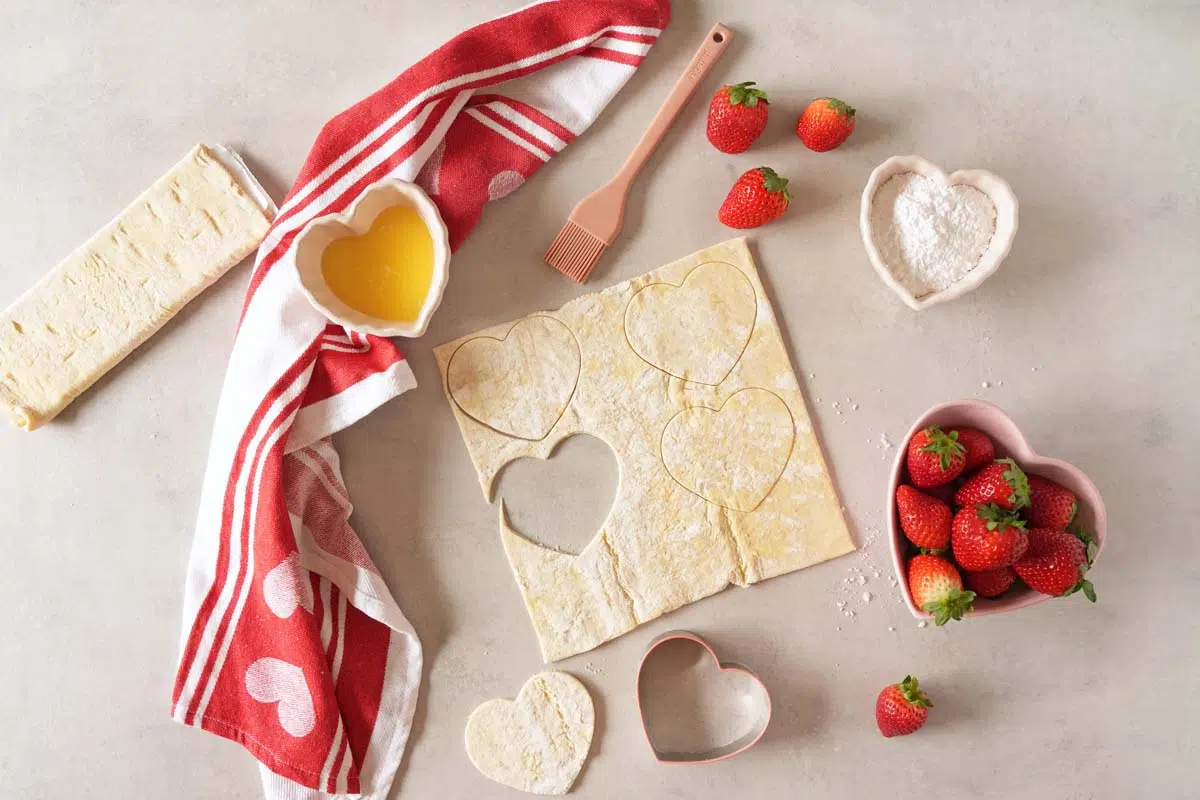 Puff pastry with heart-shaped cutouts and cream puff ingredients in heart-shaped bowls.