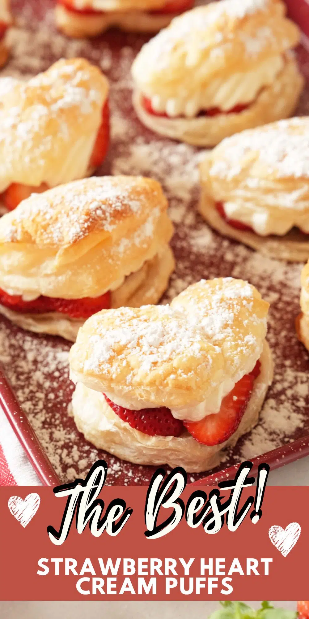 A vertical Pinterest image that features heart-shaped cream puffs on a red baking sheet. Image contains text that reads: The Best Strawberry Heart Cream Puffs.