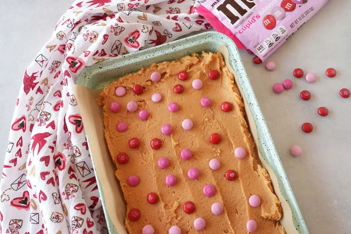 Unbaked Valentines day blondies in a blue pan with a valentine's day napkin and M&Ms nearby.