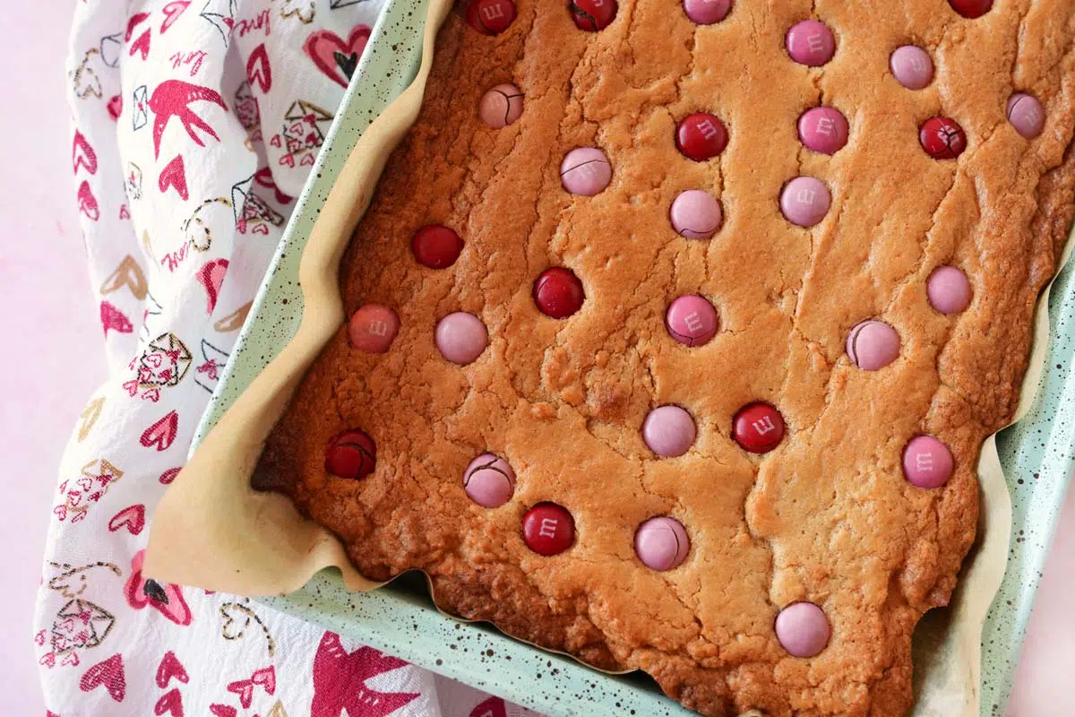 Golden brown shot of blondies with Valentines day M&Ms and a festive, heart napkin nearby.