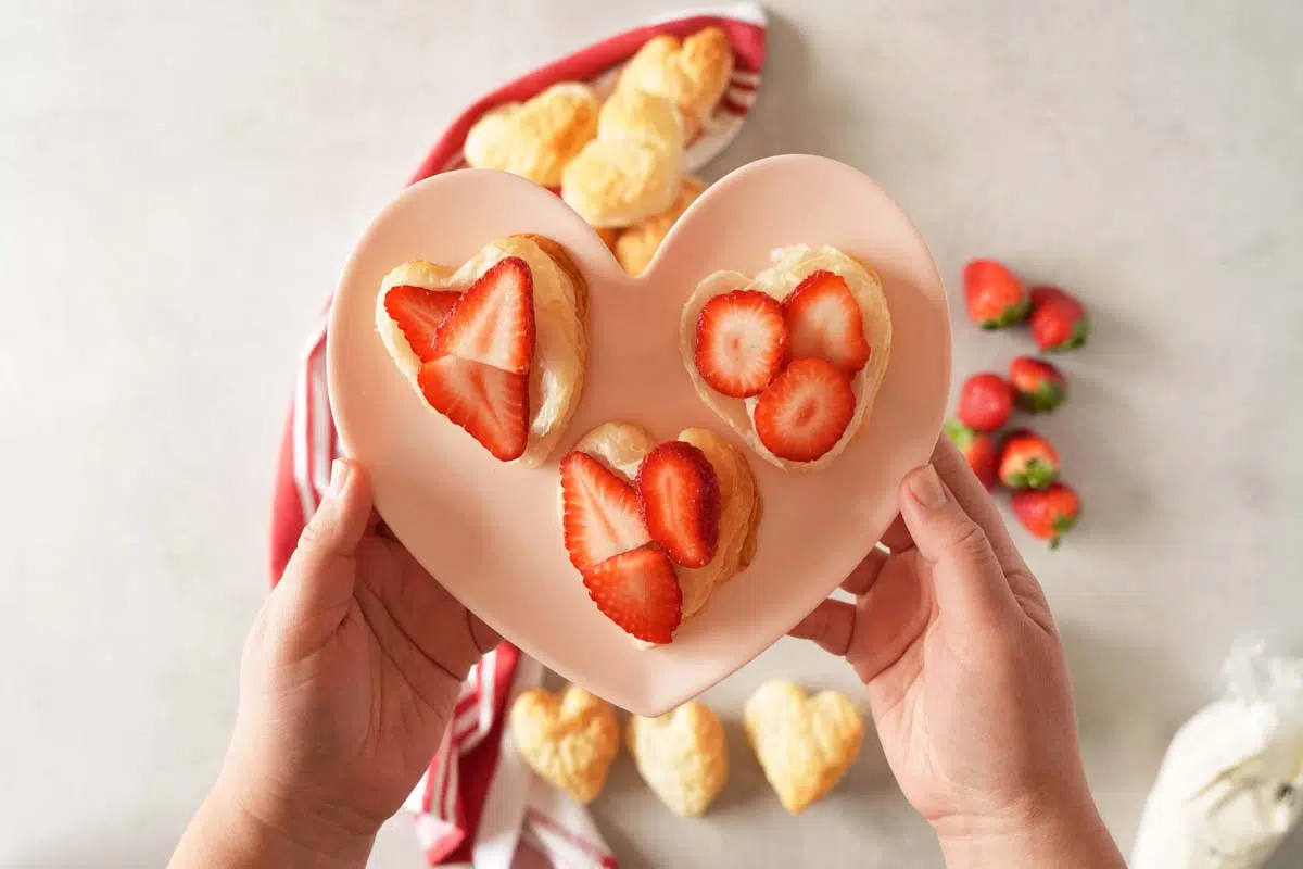 Strawberry slices on heart pastry on a heart plate being held up in hands.