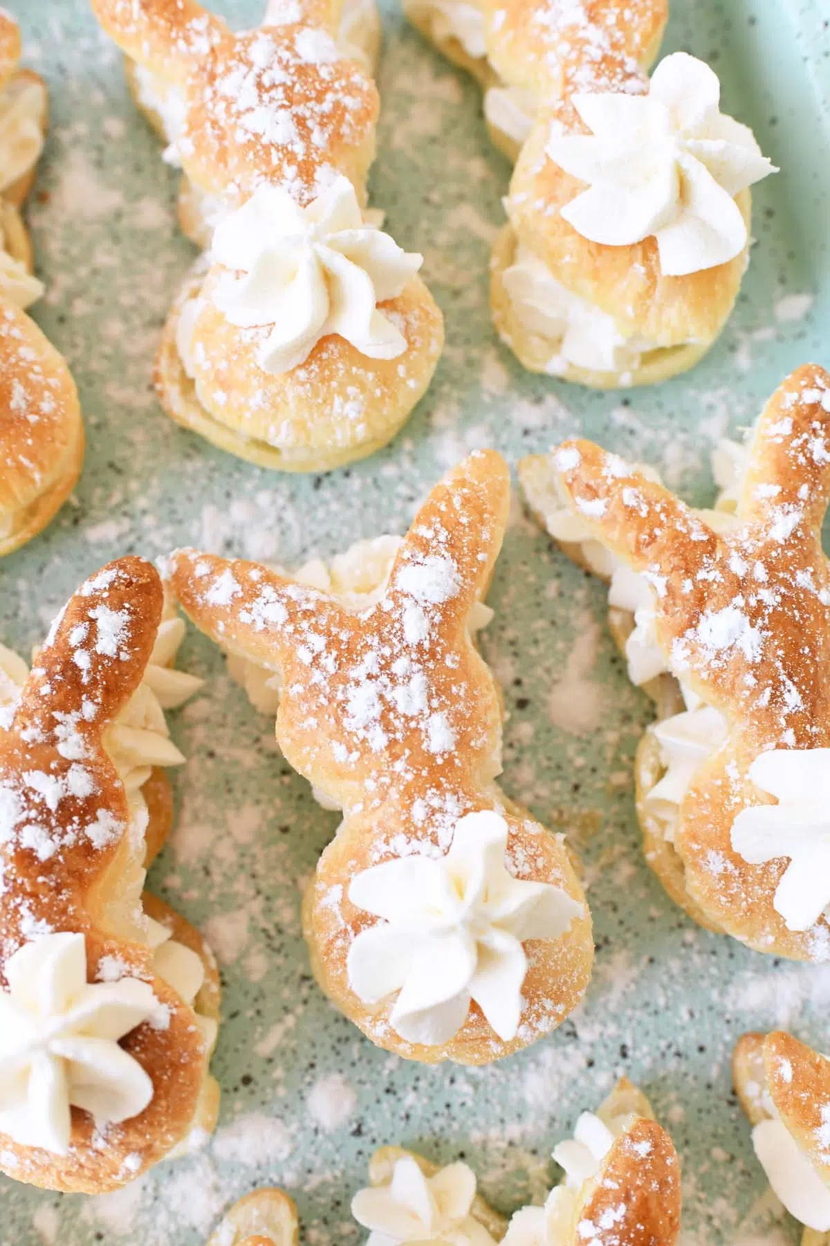 Bunny Cream Puffs with whipped cream tails on a blue, speckled pan sprinkled with powdered sugar.