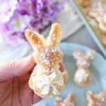 A hand holding a bunny puff pastry cream puff neat purple flowers.