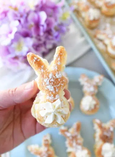 A hand holding a bunny puff pastry cream puff neat purple flowers.