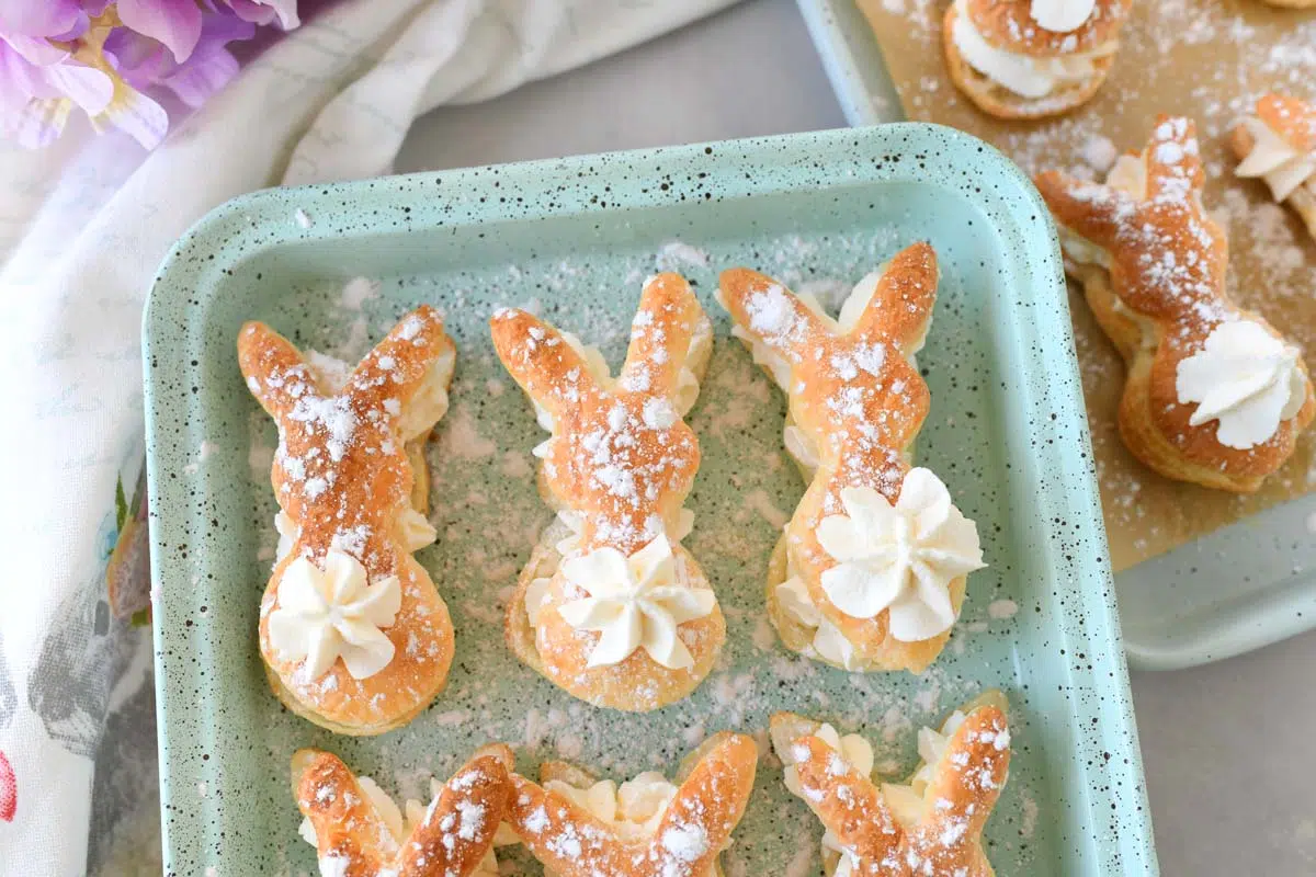 Powdered sugar-coated bunny puff pastry on a blue, speckled pan.