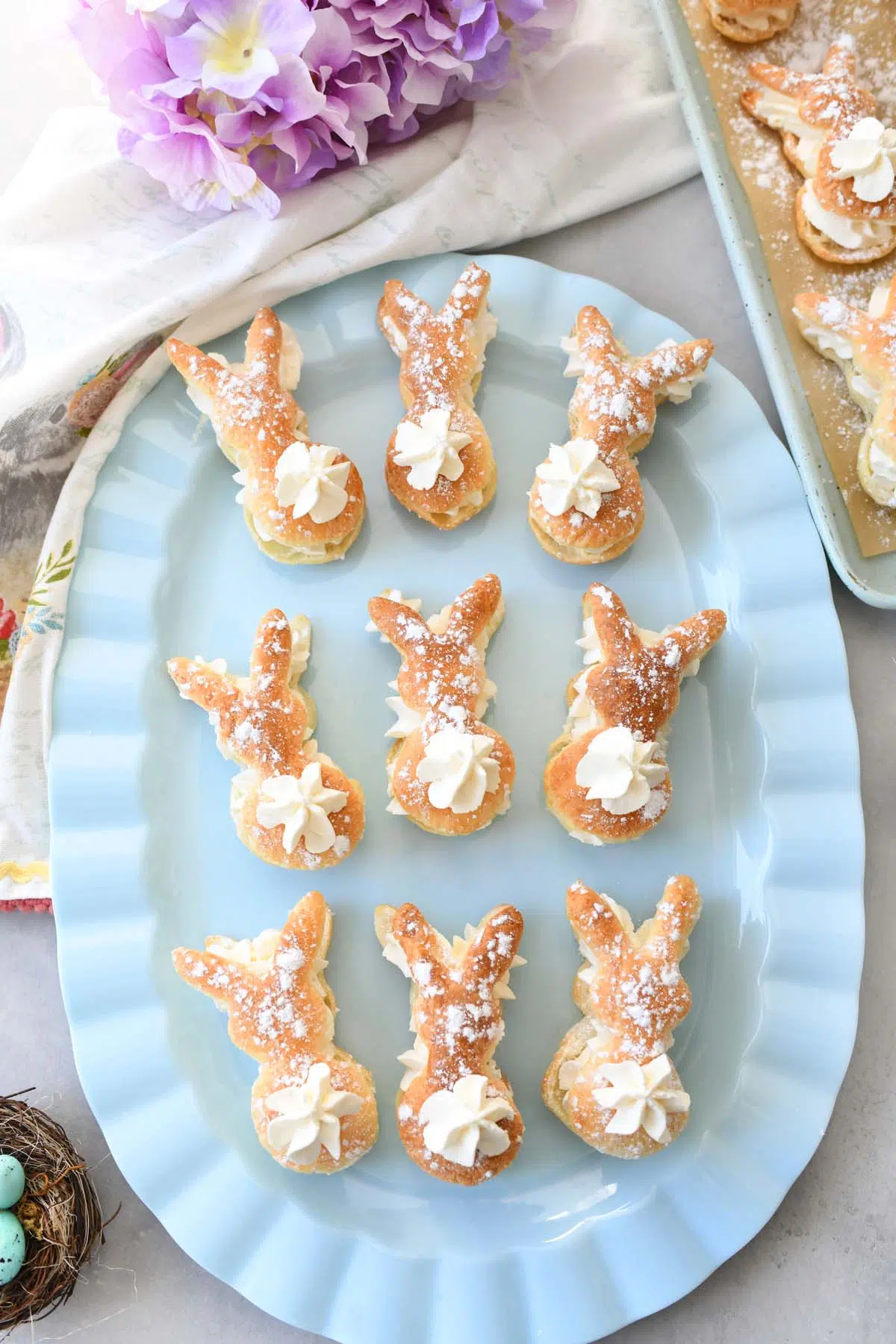 Bunny puff pastries on a blue, oval plate near purple flowers.