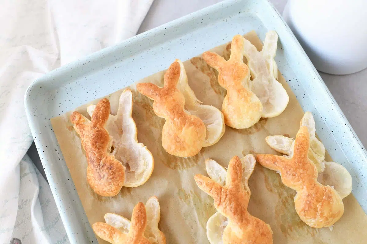 Golden brown bunny pff pastry cutouts on a parchment-lined blue baking sheet.
