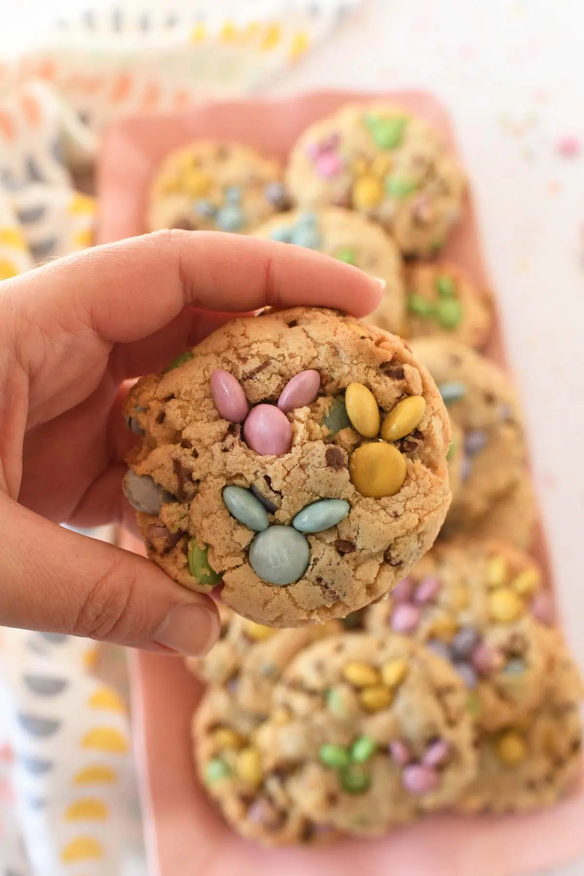A white hand holding up a baked M&M bunny cookie.