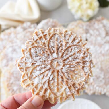 A powdered sugar coated pizzelle in a white hand.