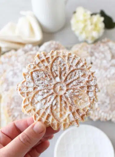 A powdered sugar coated pizzelle in a white hand.