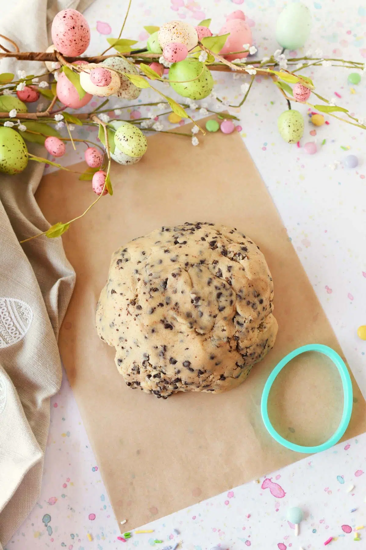 Chocolate chip cookie dough on tan parchment paper with a green, egg cookie cutter nearby.