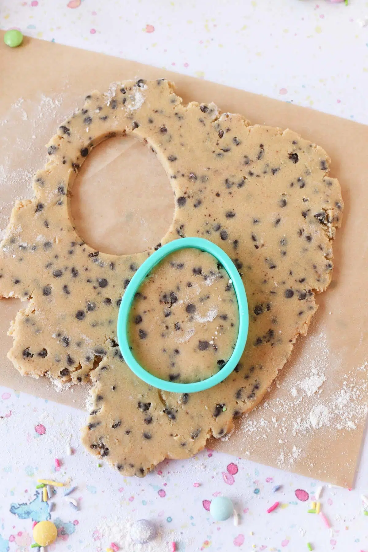 Rolled out mini chocolate chip cookie dough with a green egg cutter near the dough.