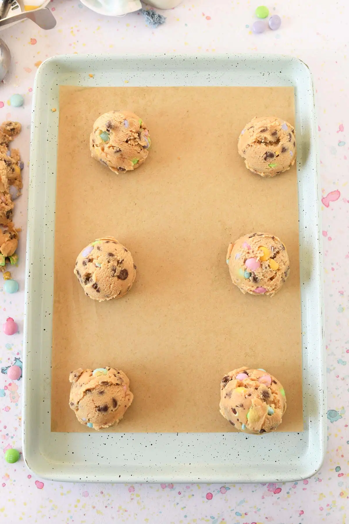 M&M Easter cookie dough balls on a parchment-lined blue, speckled baking sheet.