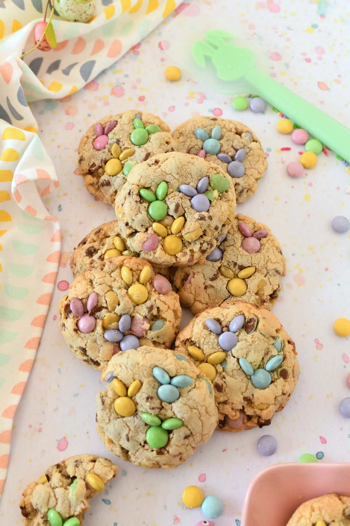 Pastel M&M bunnies on thick, chocolate chip cookies. Cookies are styled on a pastel speck surface with a pastel napkin nearby.