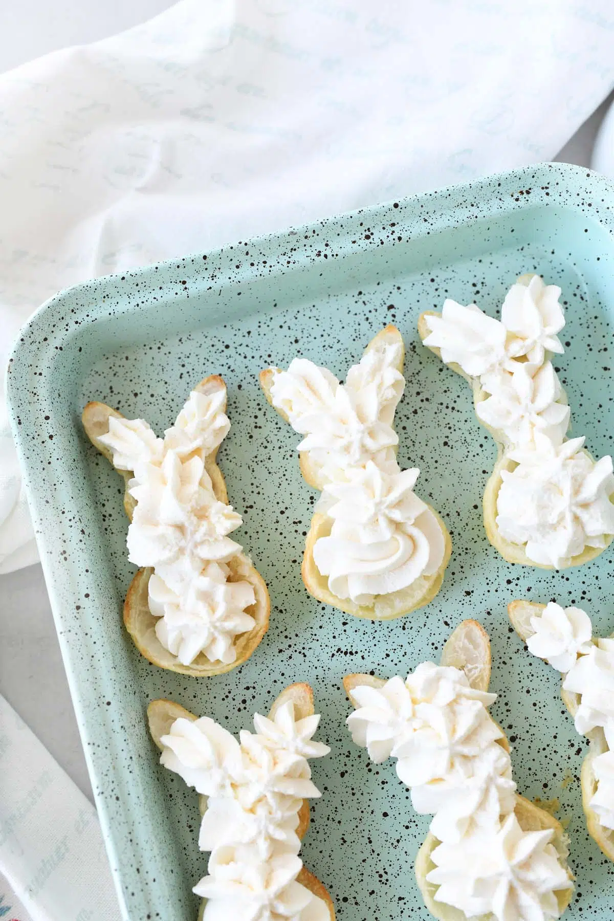 Cream puffs with whipped creamon them on a blue, speckled pan.