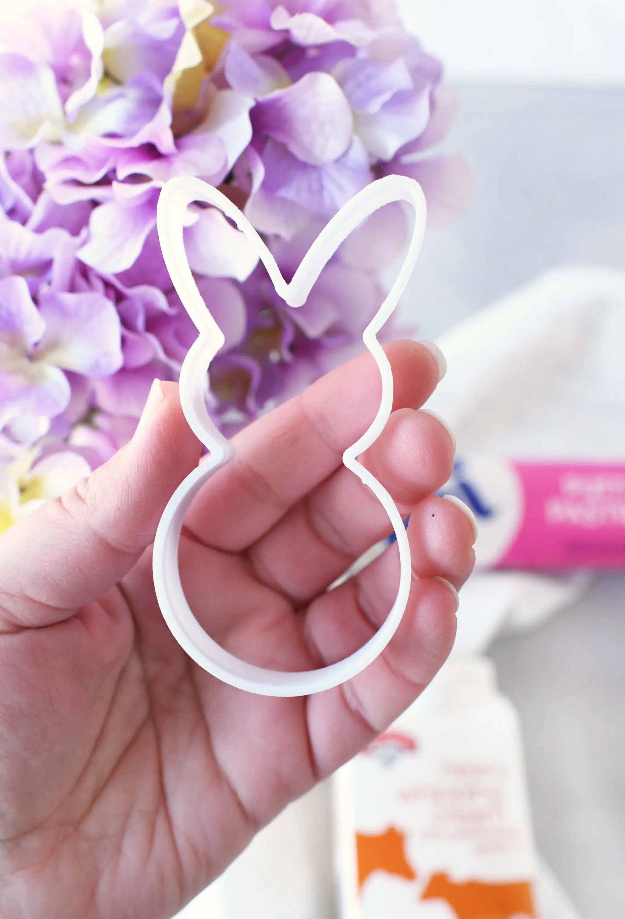 Easter bunny cookie cutter in a hand near purple flowers.