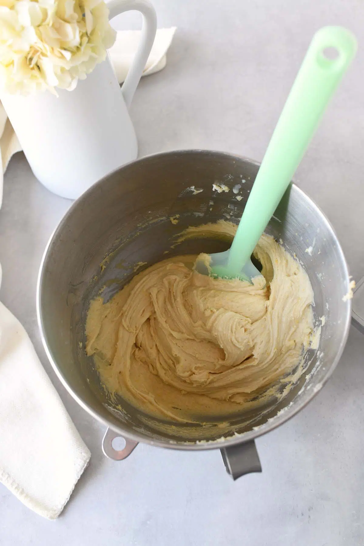 Thick pizzelle dough in a stainless steel bowl with a green spatula.