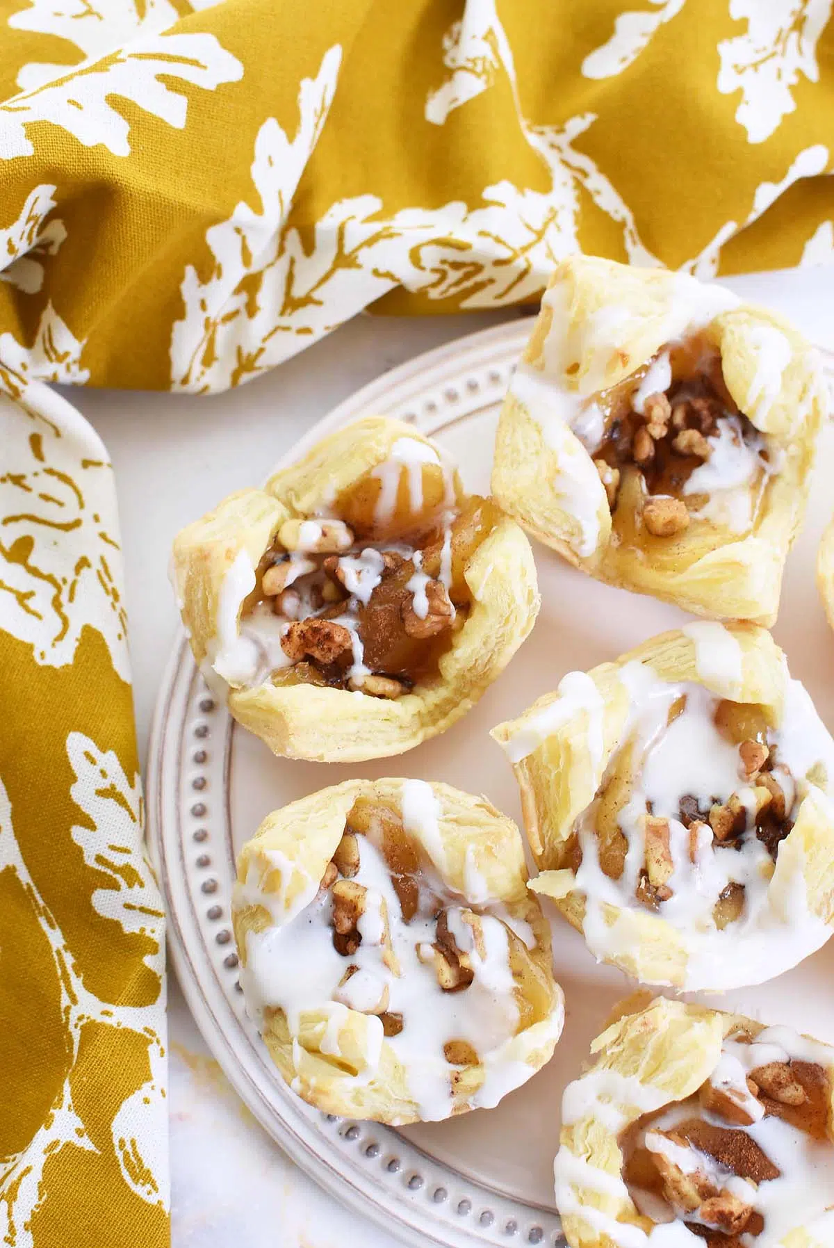 Iced puff pastry apple pies on a white tray with a fall napkin nearby.
