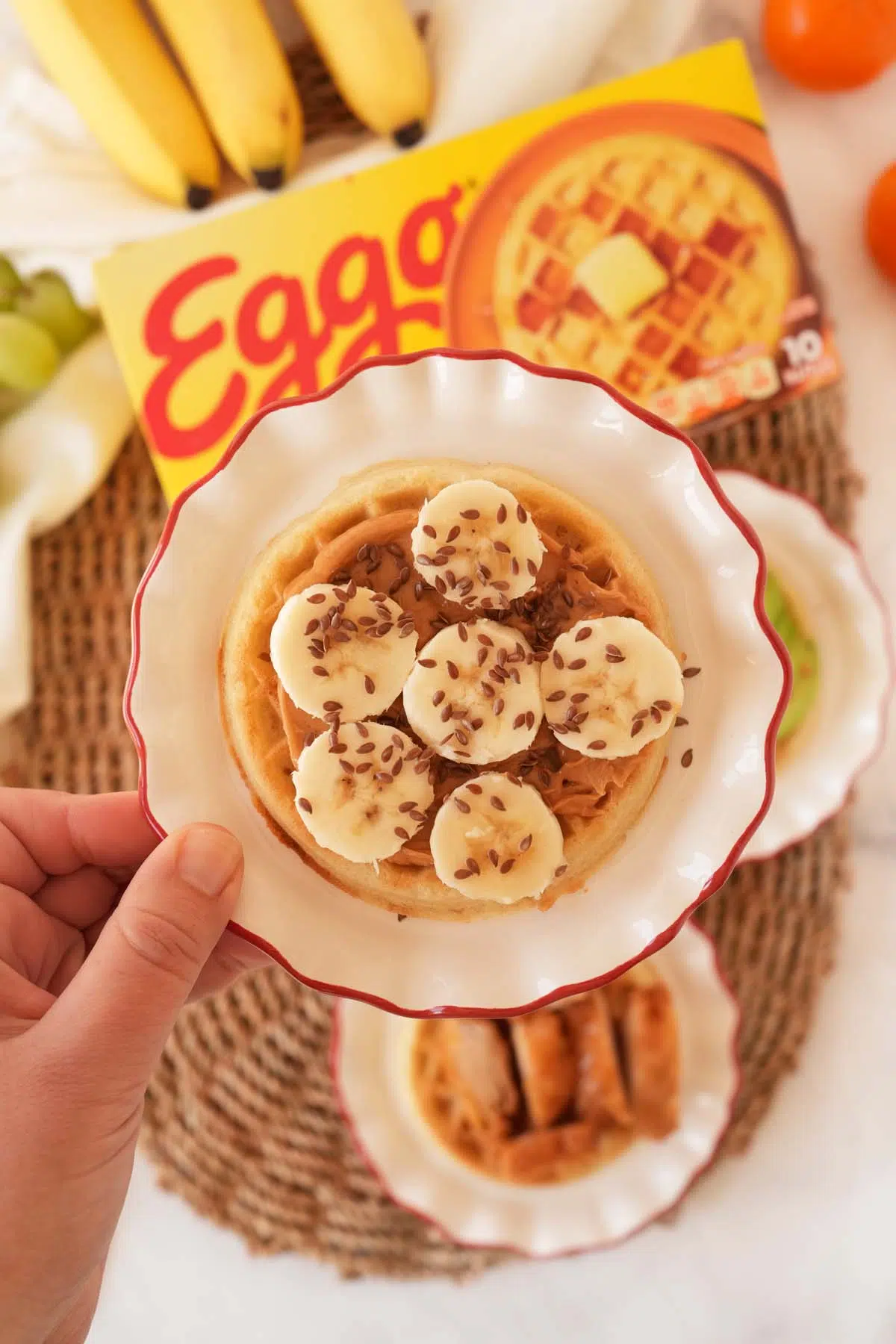 Banana with peanut butter, banana, and flax seeds near a box of Eggo waffles.
