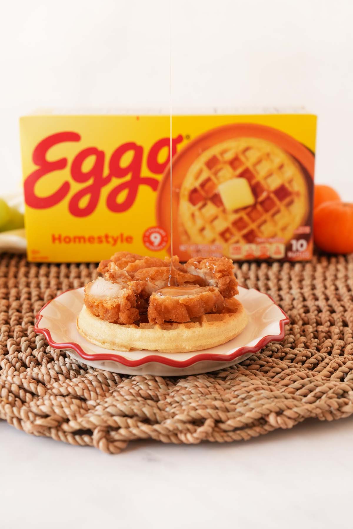 Syrup drizzling on chicken on an Eggo waffles near a yellow box of Eggo Waffles.