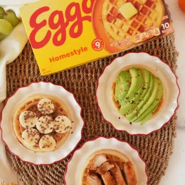Eggo waffles box near fresh fruit, and 3 plates with various topped waffles.