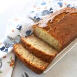 Sliced sour cream banana bread on a white plate near a blue chicken napkin.